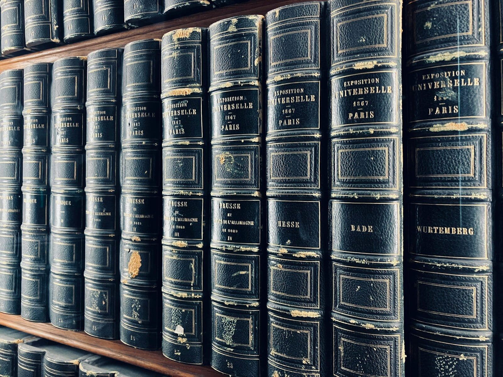 a row of black books sitting on top of a wooden shelf